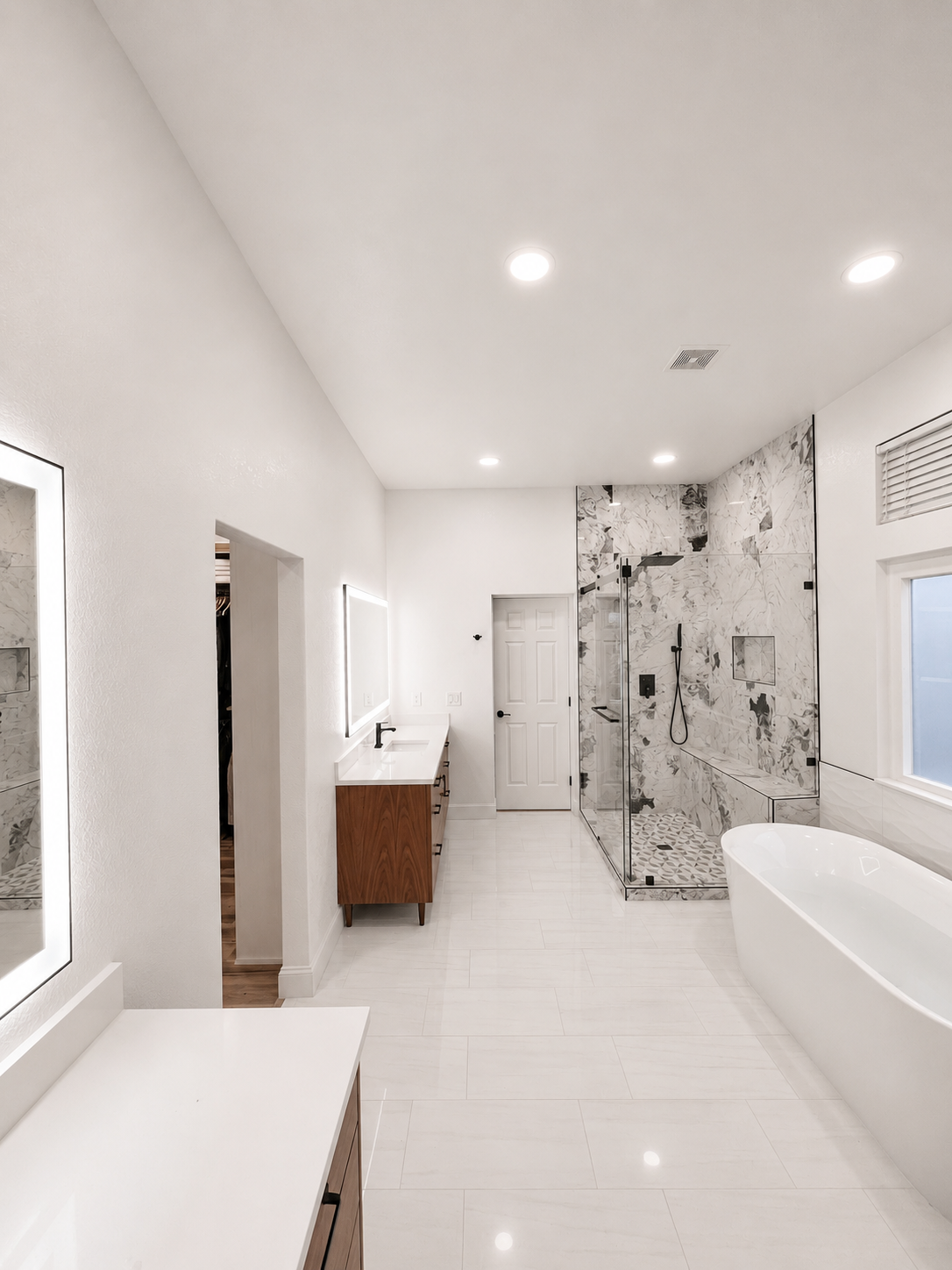 Bright modern bathroom with white tile, vanity, large mirror, and glass shower enclosure