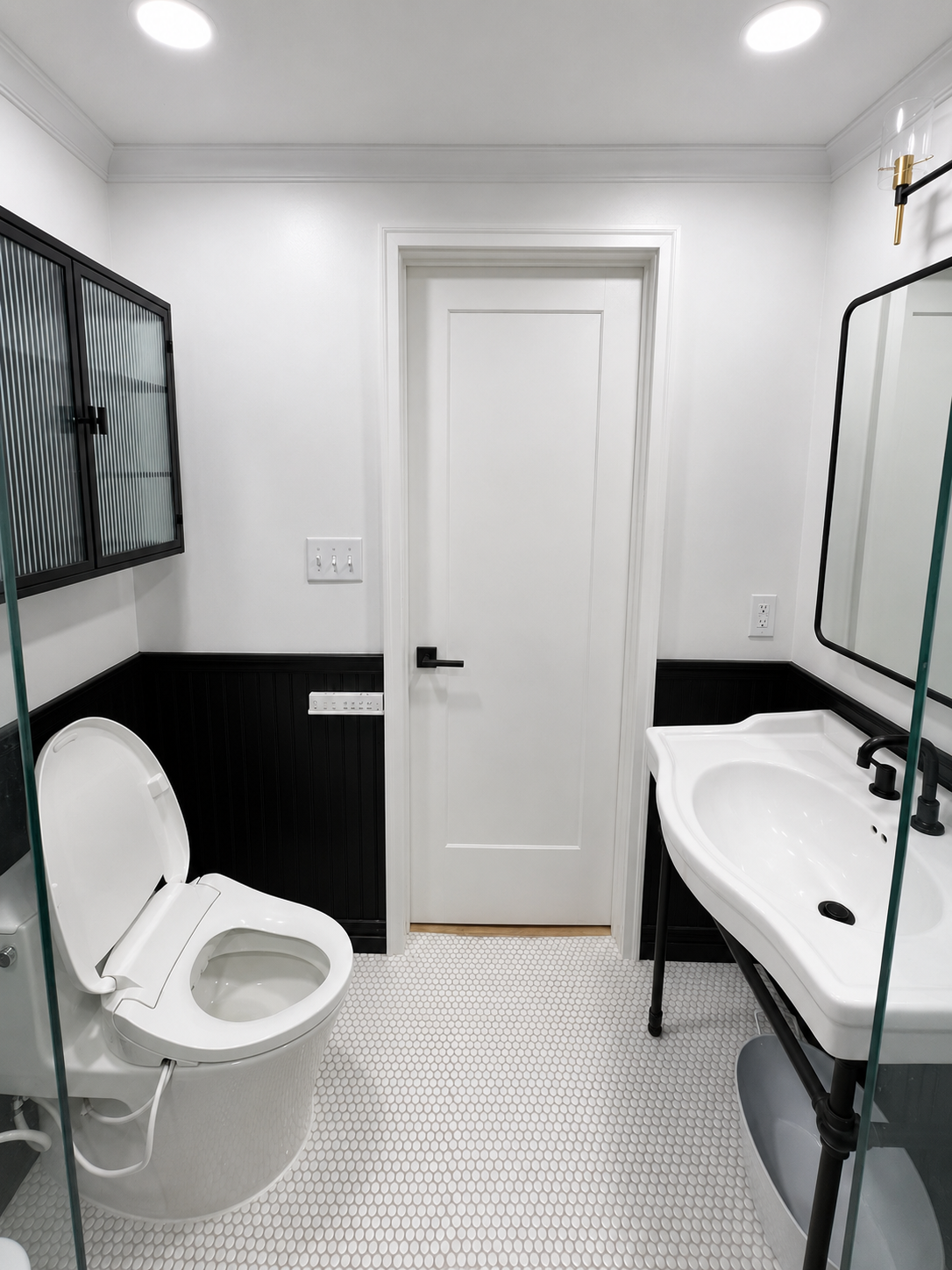 Small bathroom with white toilet, sink, mirror, and closed door, black-and-white walls and patterned floor.