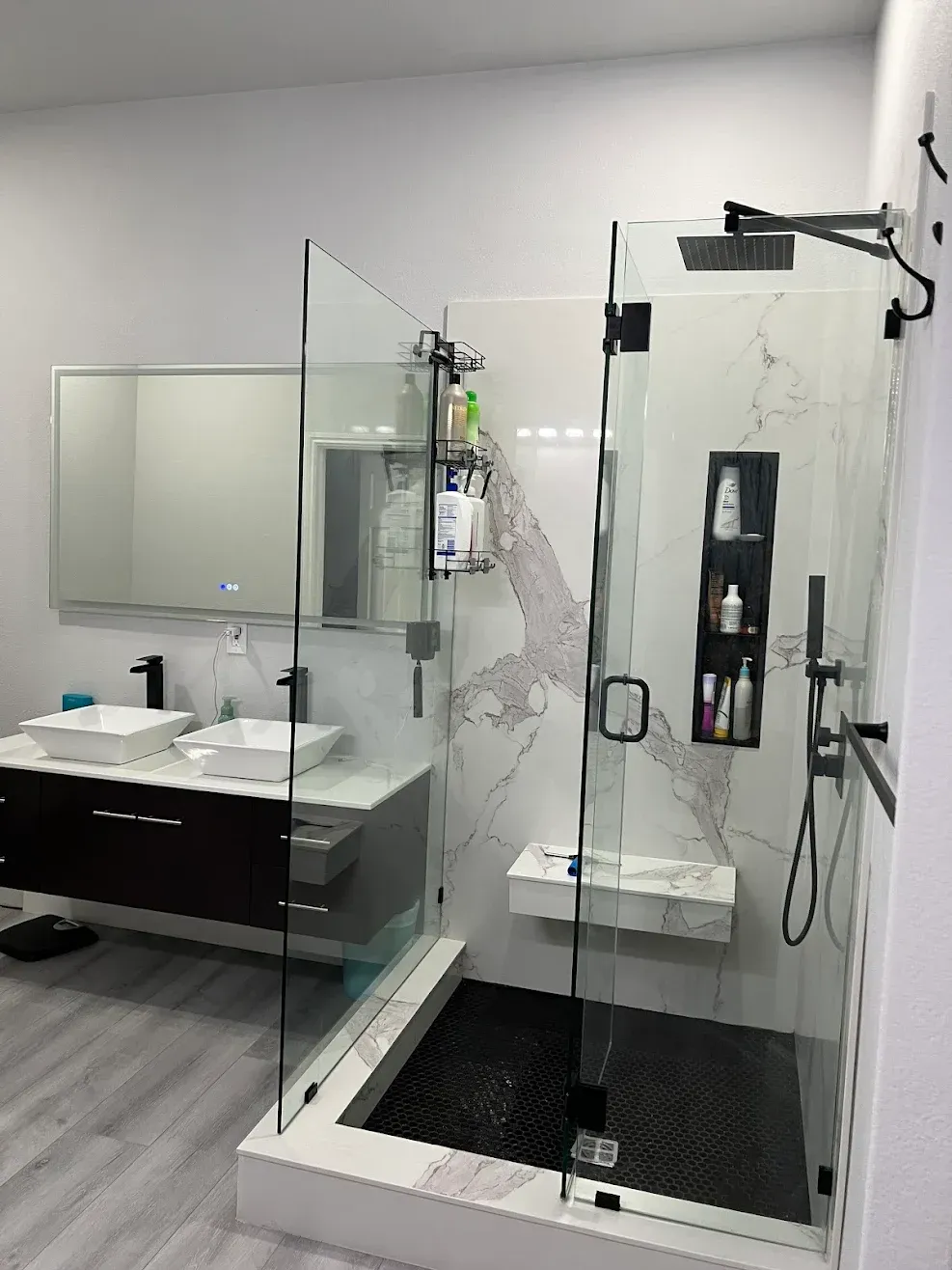 Modern bathroom with glass shower, black shower mat, and vanity sink with mirror on the left