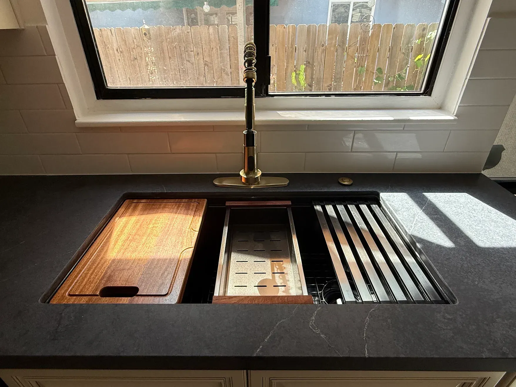 Kitchen sink with black countertop, gooseneck faucet, and a sunlit window above a drying rack.