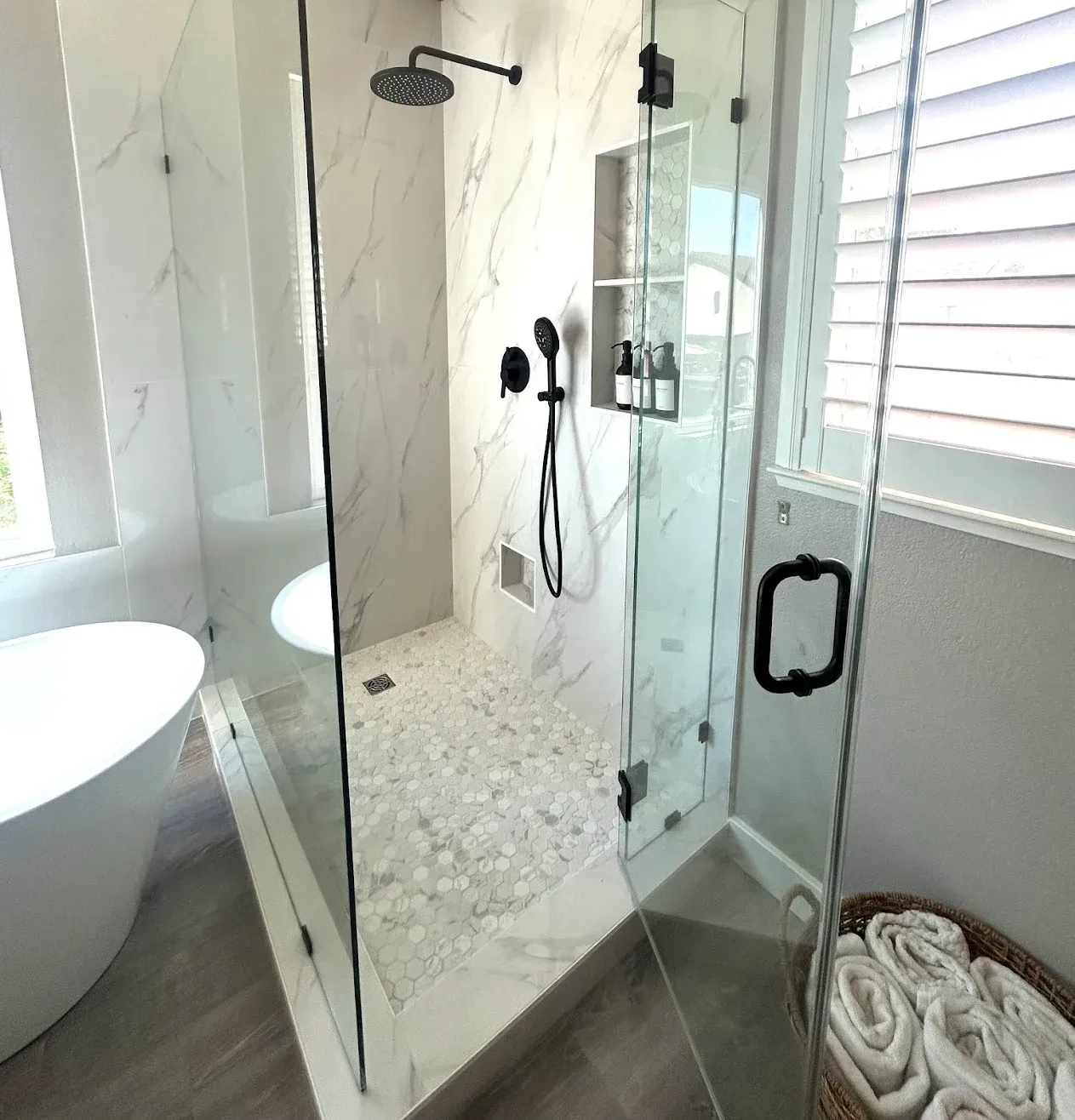 Modern bathroom with glass shower, freestanding tub, and rolled towels on the floor