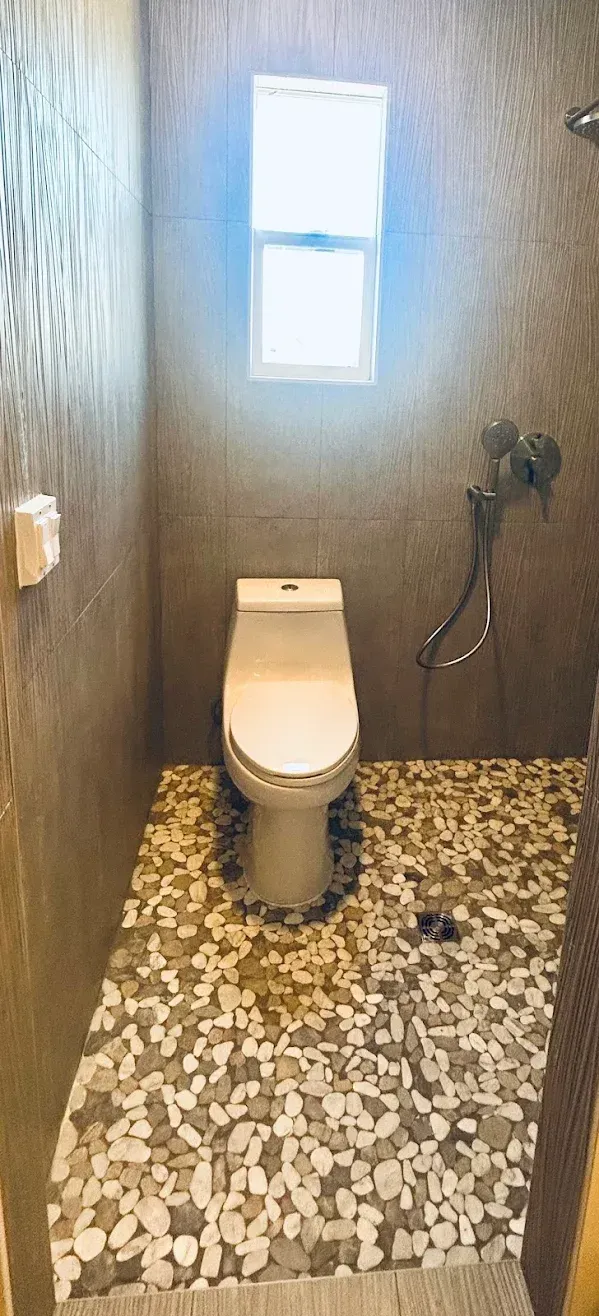 Small restroom with toilet, mosaic floor, dark wood walls, and frosted window above.