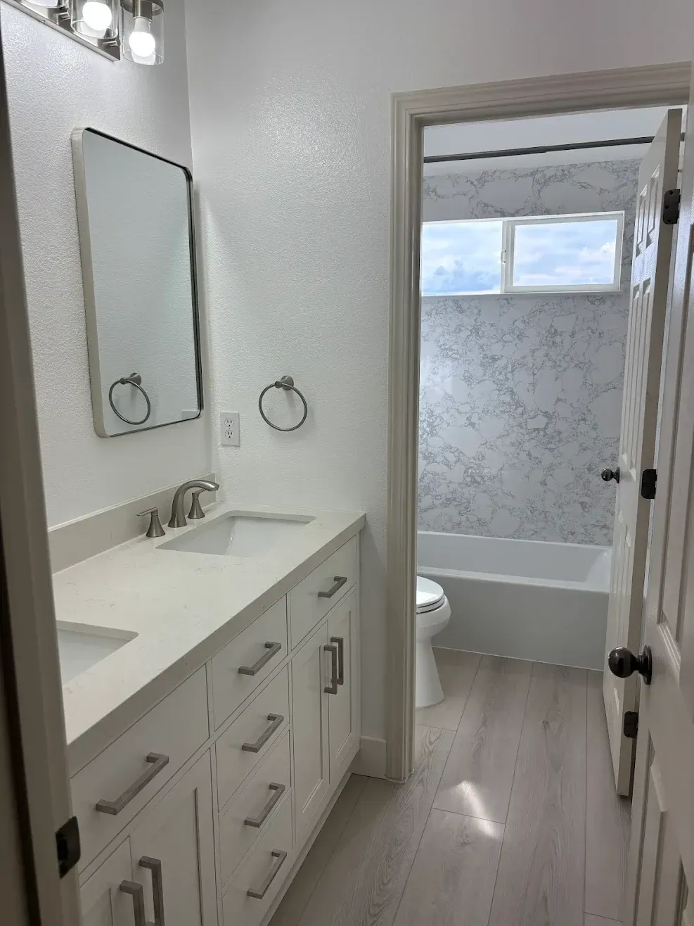 Bright white bathroom vanity with mirror and sink leading to a small tiled shower room.