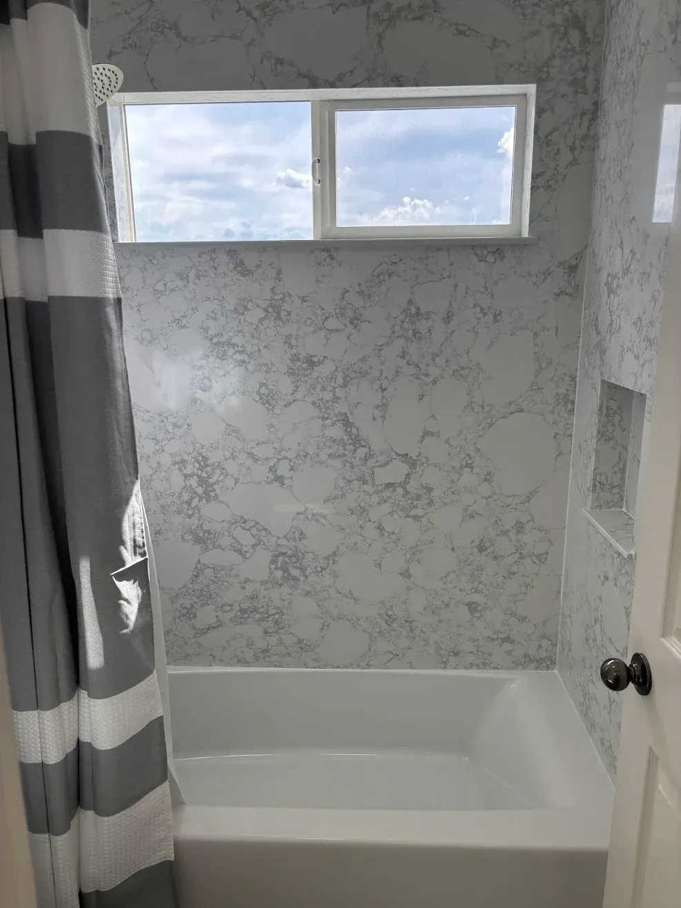 Small bathroom with a white bathtub, patterned gray wallpaper, and a narrow window above the tub.