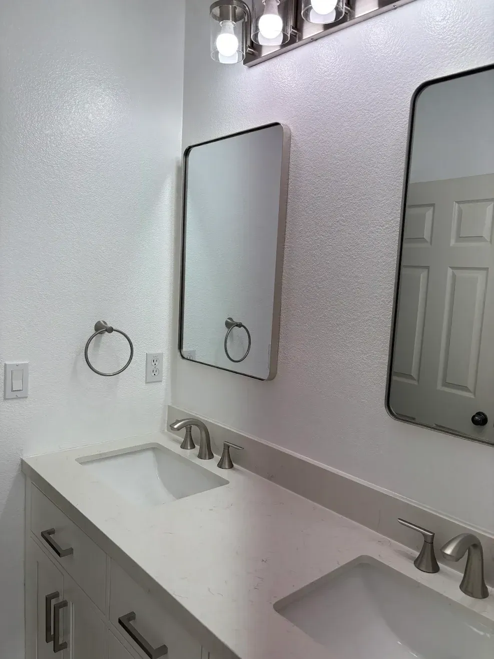 Modern bathroom with two sinks, mirrors, wall sconces, and a towel ring