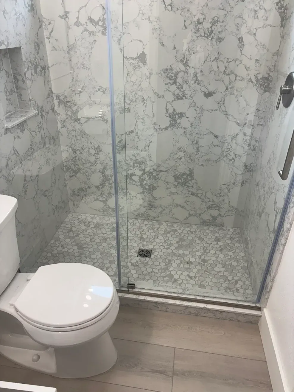 Modern bathroom with a toilet and a glass-enclosed shower with marble-patterned tile.