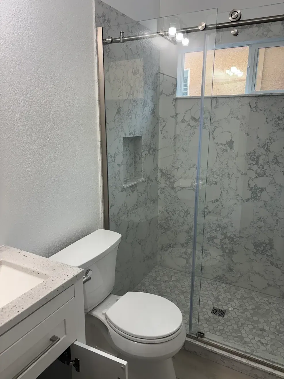 Modern bathroom with a toilet beside a glass shower enclosure and frosted window.