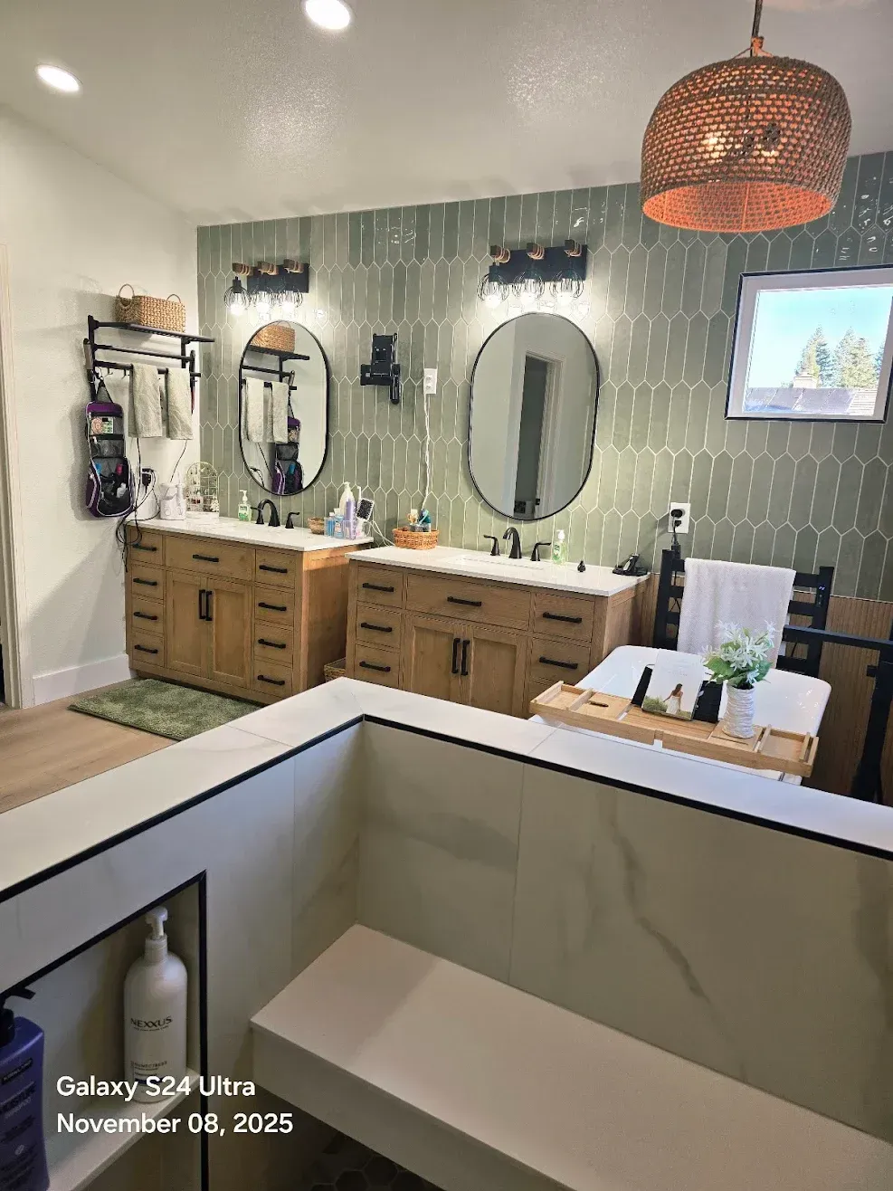 Modern bathroom with double vanity, round mirrors, tiled wall, and freestanding tub in foreground