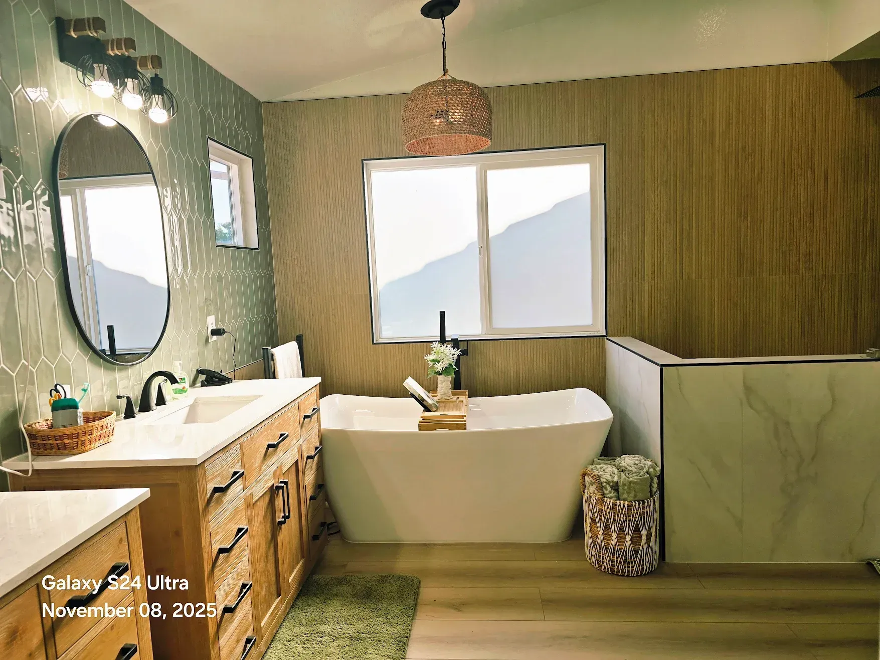Spa-like bathroom with wood vanity, freestanding tub, round mirror, and mountain view window
