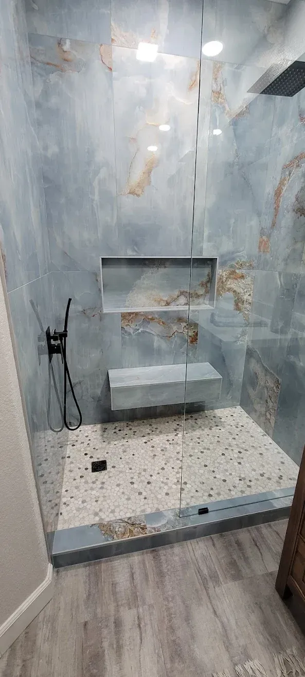 Blue-gray tiled walk-in shower with built-in bench and pebble floor, viewed from the doorway