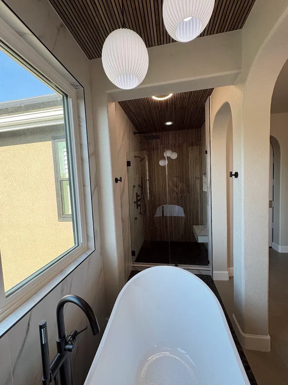 Modern bathroom with freestanding tub, arched doorway, wood accents, and pendant lights