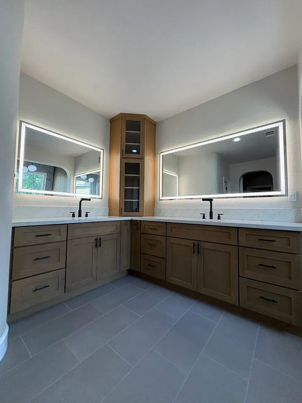 Bathroom vanity with double sinks, large mirrors, wooden cabinets, and gray tile flooring.