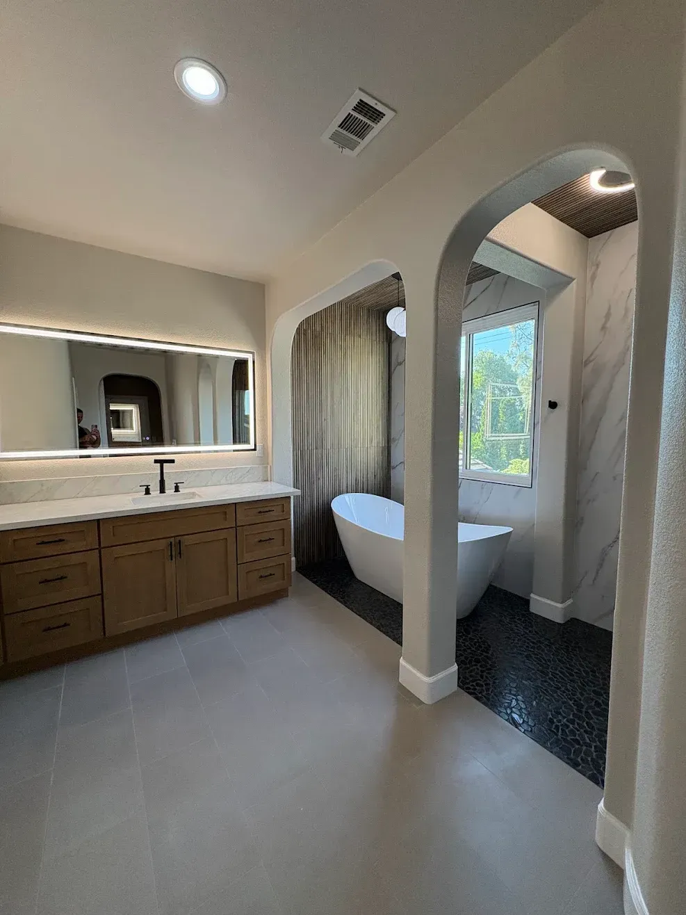 Bright bathroom with double vanity, large mirror, bathtub alcove, and window with curtains.