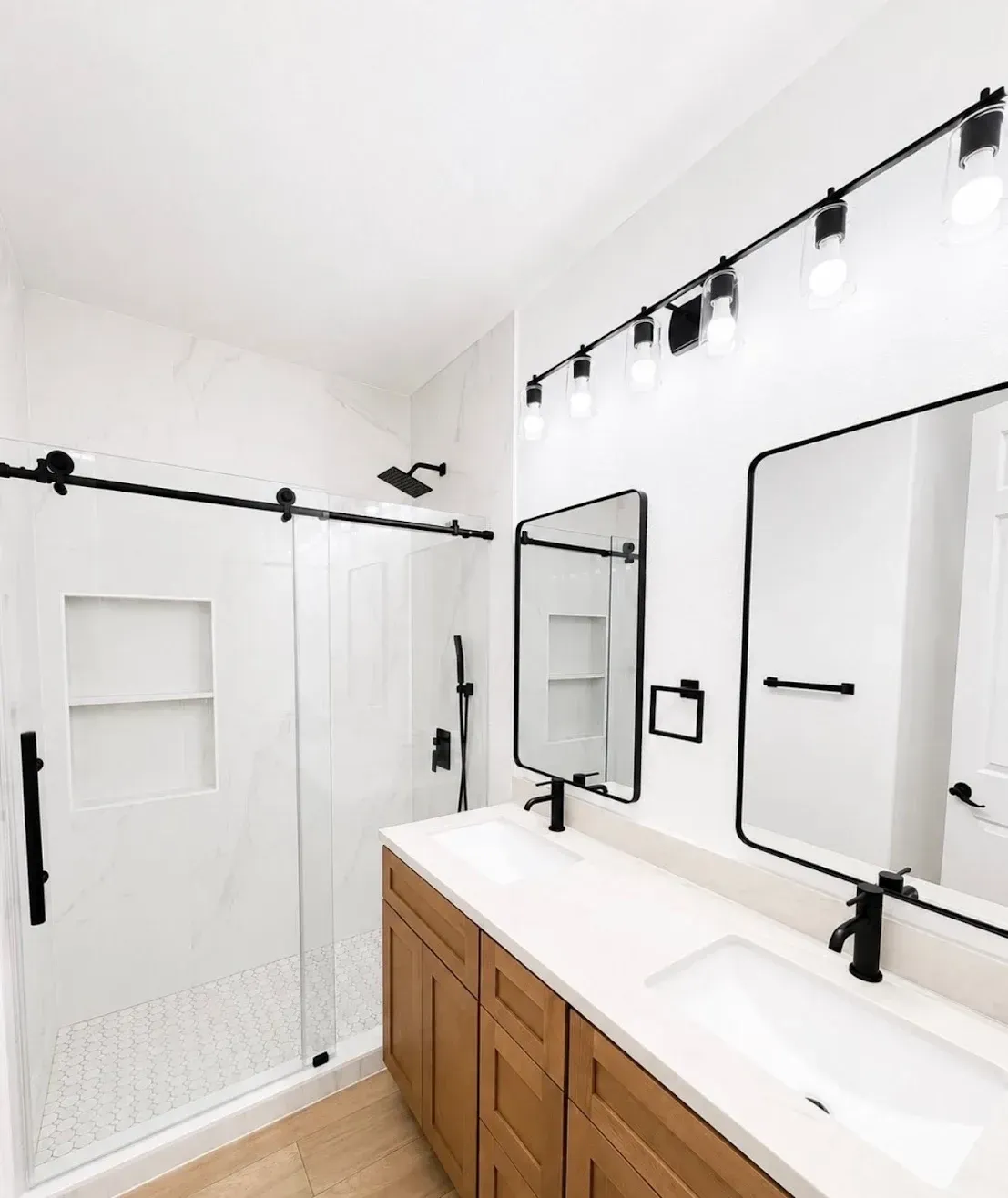 Bright modern bathroom with white shower walls, wooden vanity, and large mirror lights
