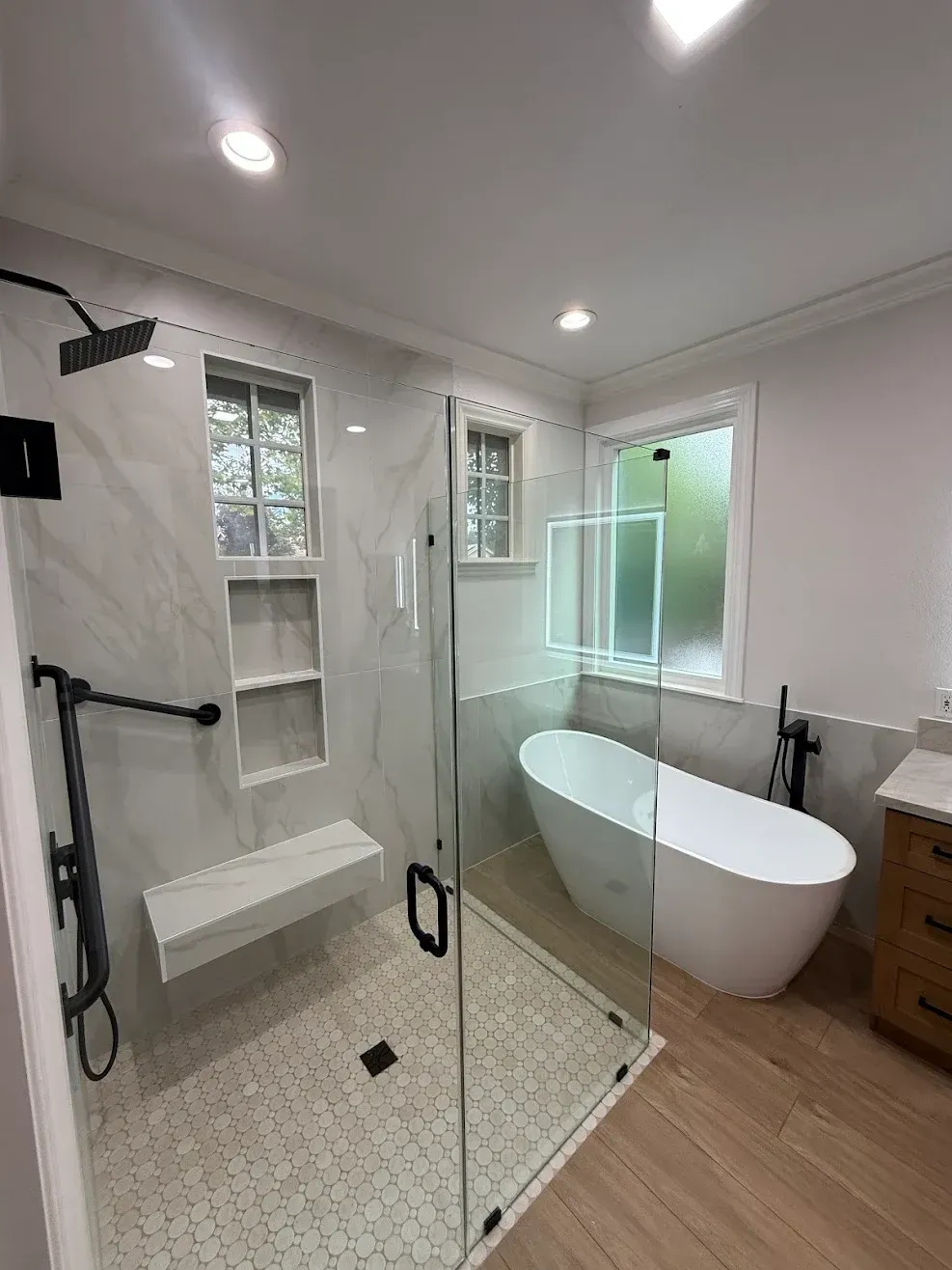 Modern bathroom with glass shower, freestanding tub, white tile, and wood flooring