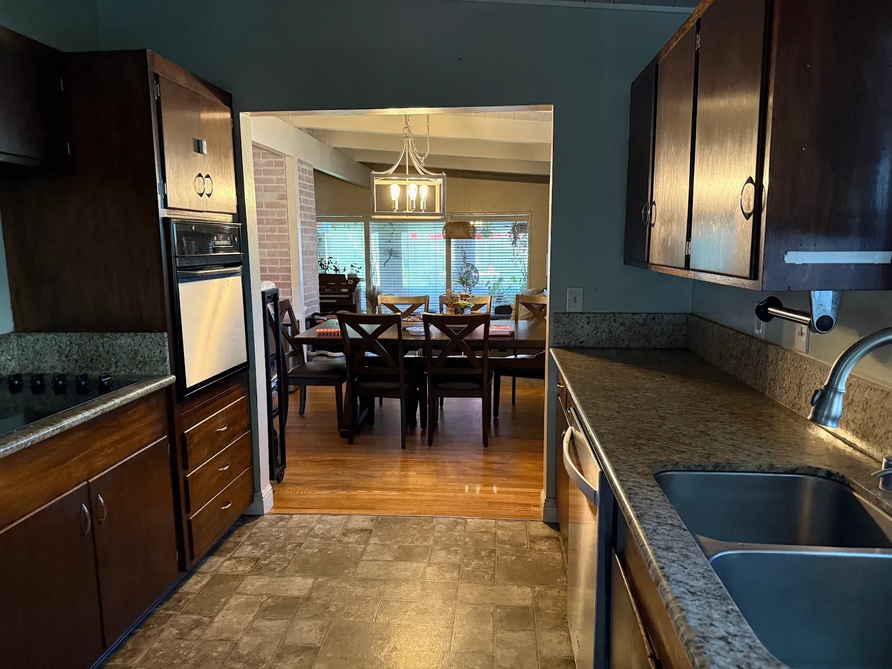 Kitchen looking into a dining room with dark wood cabinets, granite counters, and a set dining table.