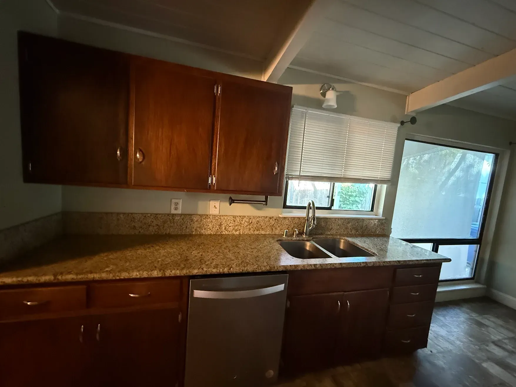 Kitchen with dark wood cabinets, granite countertop, sink, and dishwasher by a window and sliding glass door