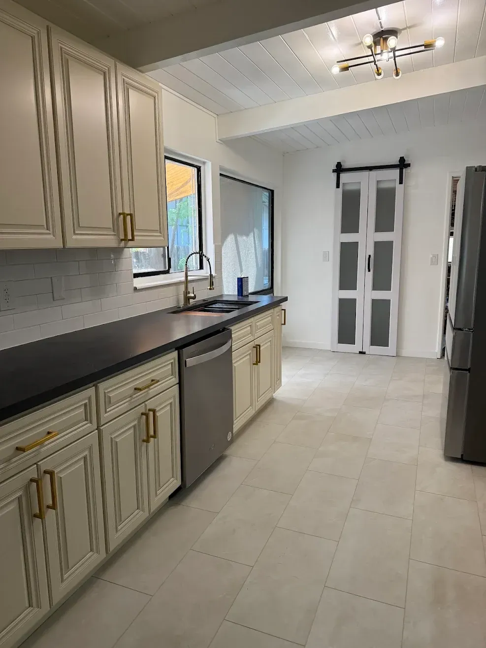 Bright kitchen with cream cabinets, black countertops, stainless appliances, and white double doors at the end.
