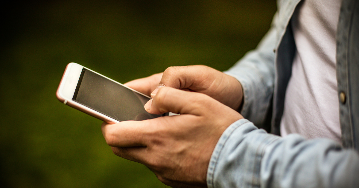 Hands holding a smartphone outdoors with a blurred green background