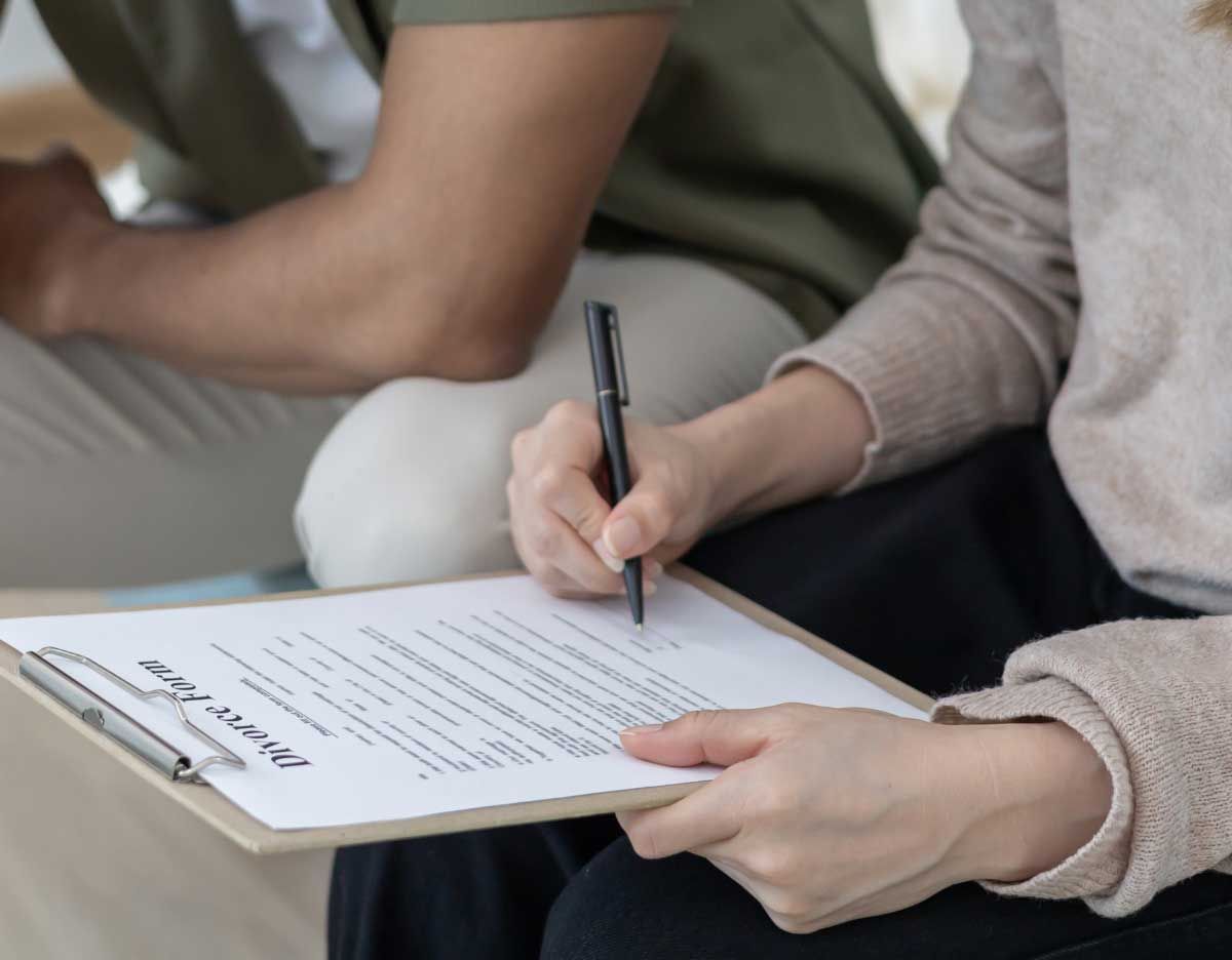 Person writing on a clipboard while seated beside another person in a casual setting Person writing on a clipboard while seated beside another person in a casual setting