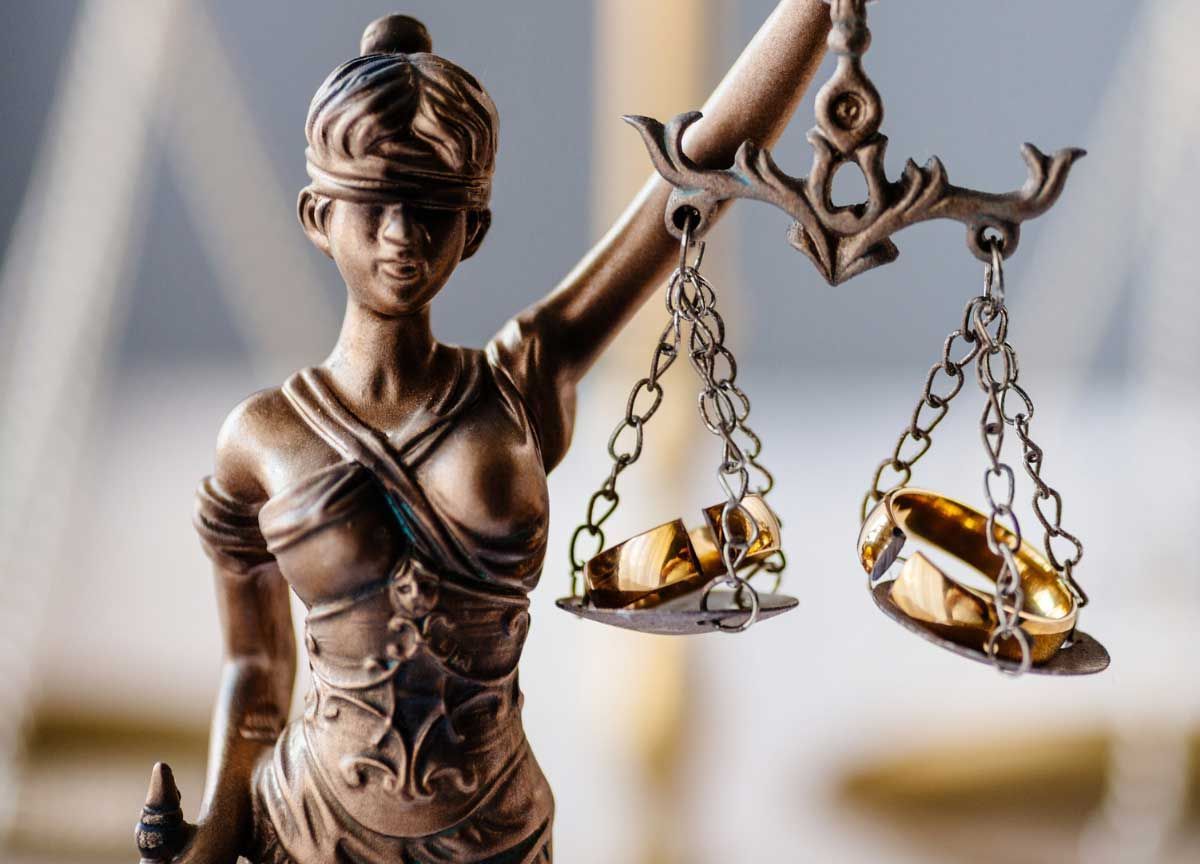 Bronze Lady Justice statue with scales against a blurred courthouse background