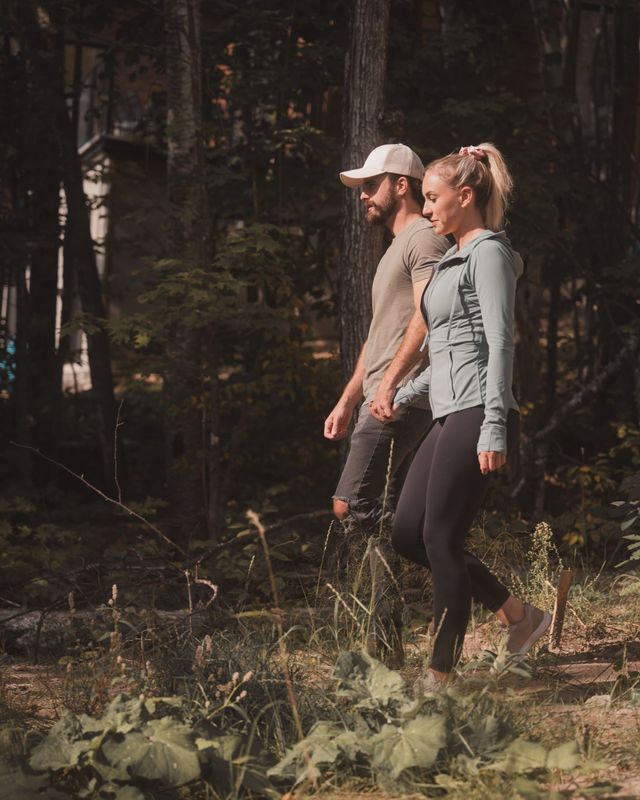 Two hikers walking through a forest clearing, one in a white cap and the other in a light jacket.