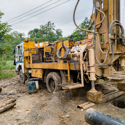 A yellow truck is parked in the dirt next to a pipe