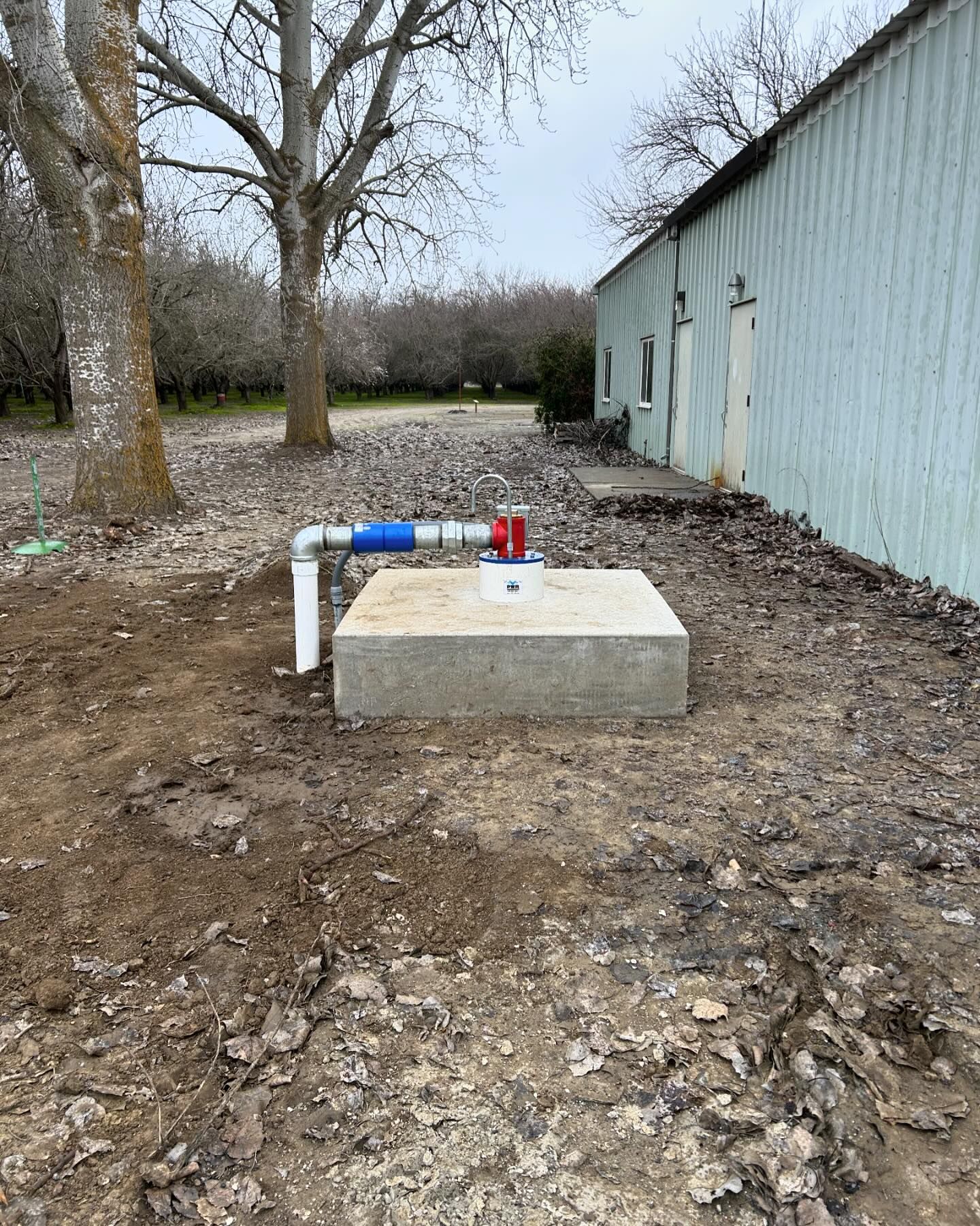 A water pump is sitting in the dirt in front of a building.
