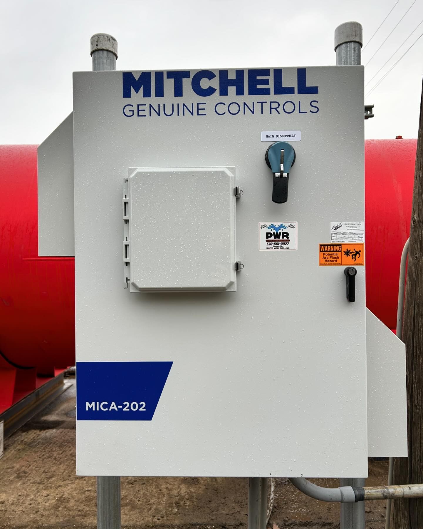 A mitchell genuine controls control panel with a red tank in the background