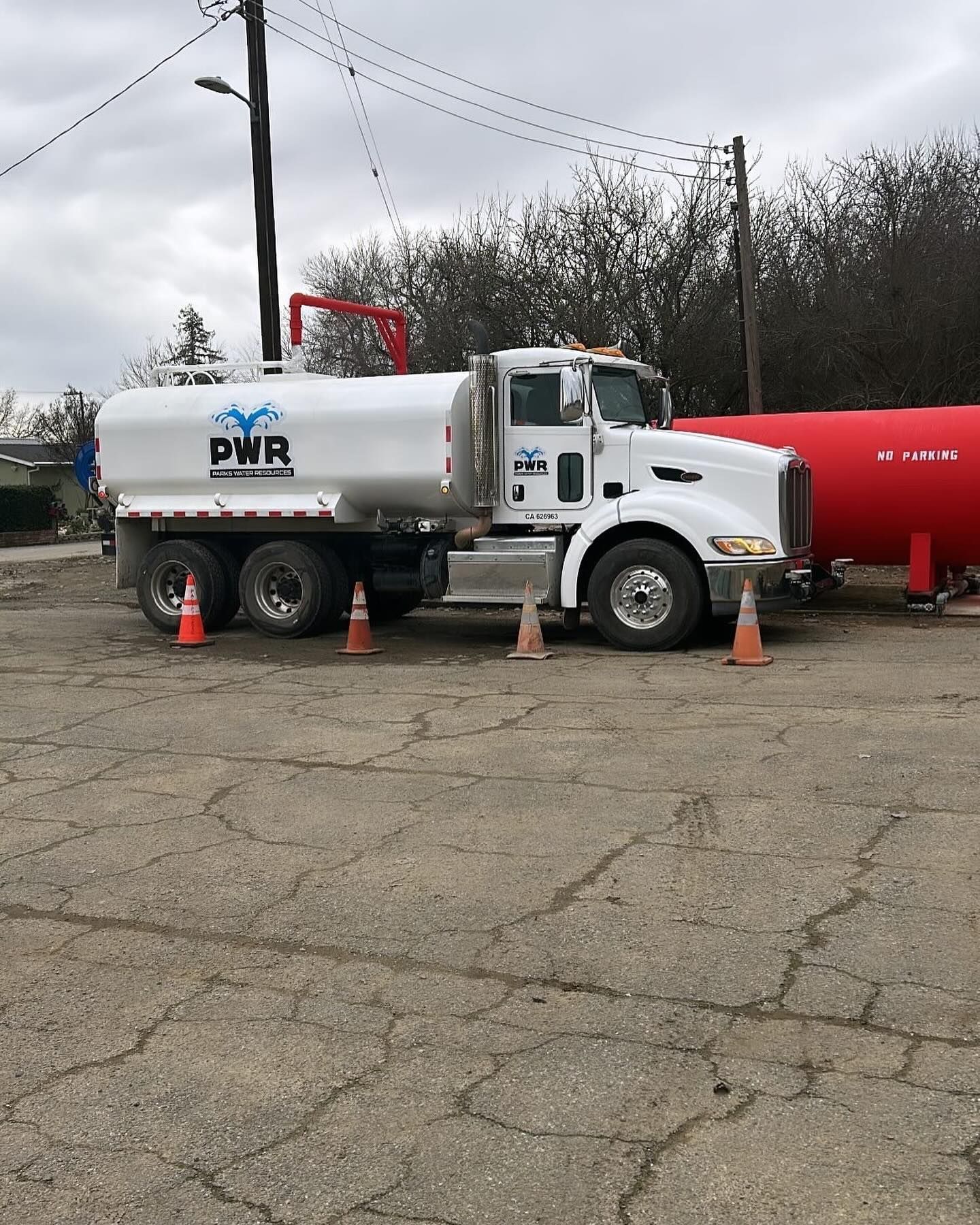 A white truck with pwr written on the side is parked next to a red tank.