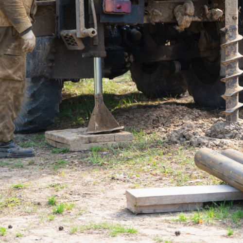 A man is standing in front of a truck with a drill in the ground.