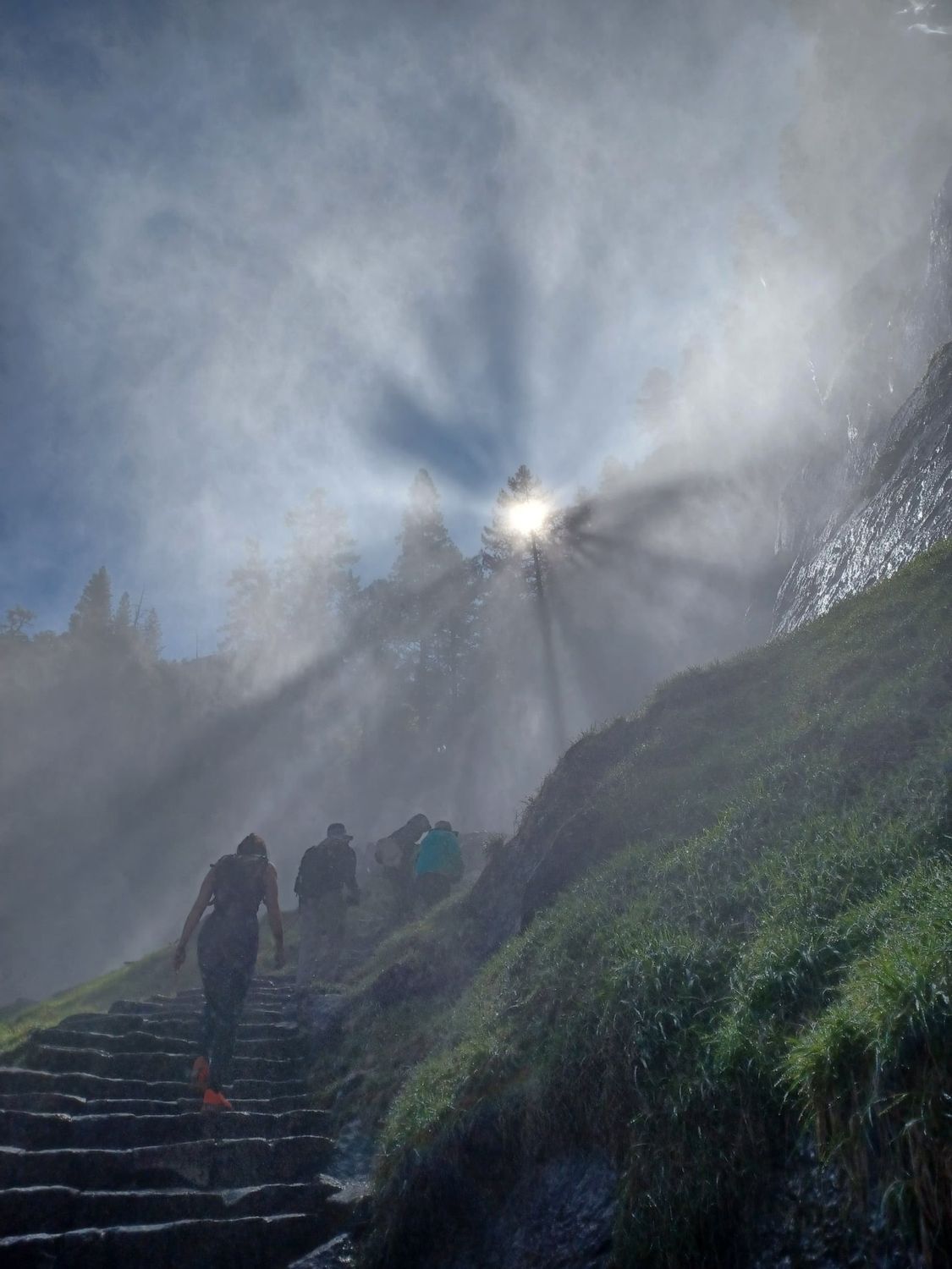 Des randonneurs gravissent des marches de pierre mouillées à travers la brume, en direction d'un éclatant rayon de soleil sur le flanc d'une montagne.