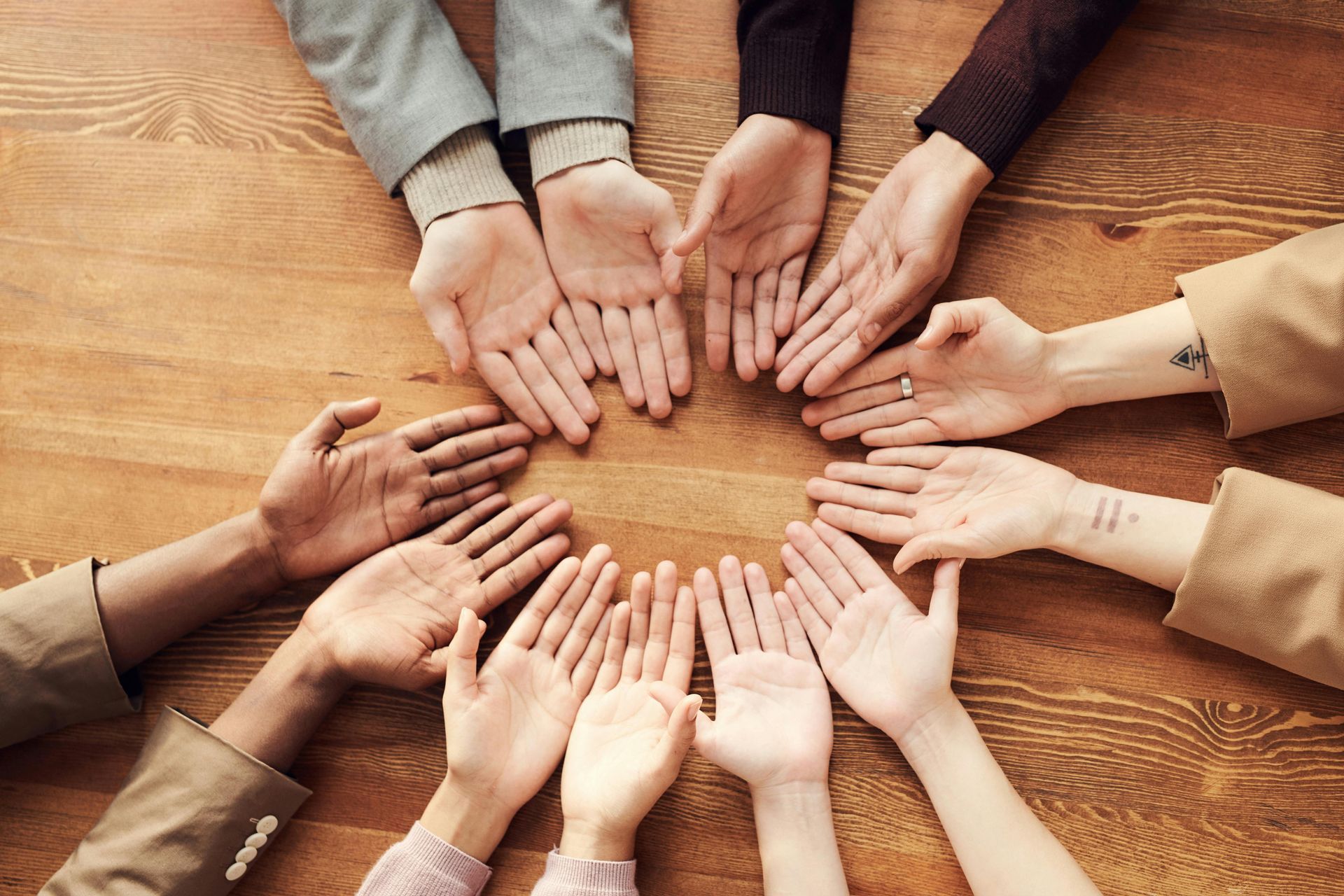 Les mains de plusieurs personnes jointes en cercle sur une table en bois.