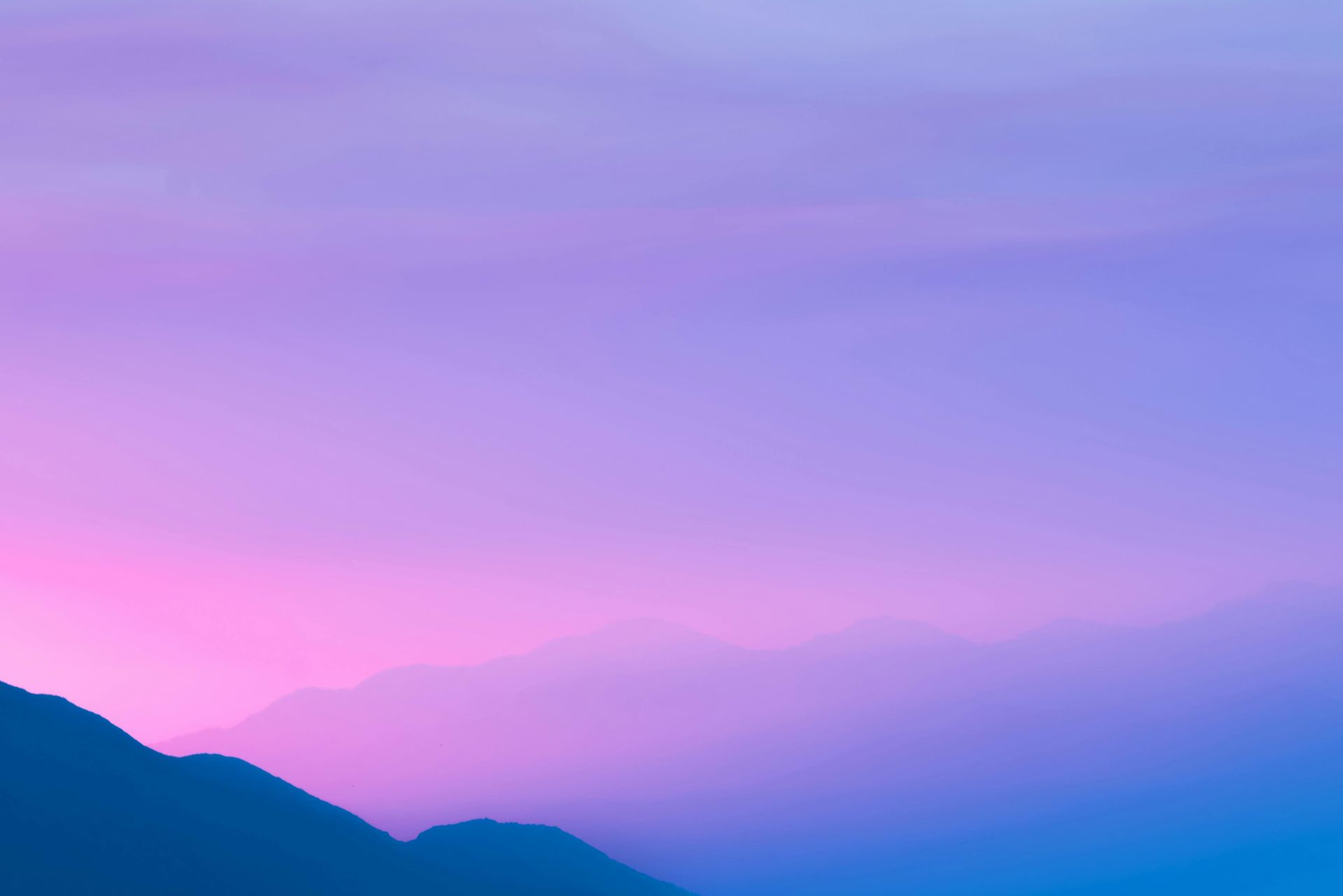 Des montagnes se découpent sur un ciel aux douces nuances dégradées de violet et de rose.