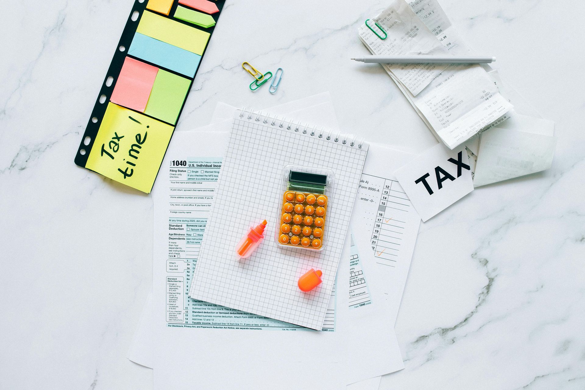 Tax preparation supplies: calculator, notepad, forms, sticky notes, receipts, and a pen on a marble surface.