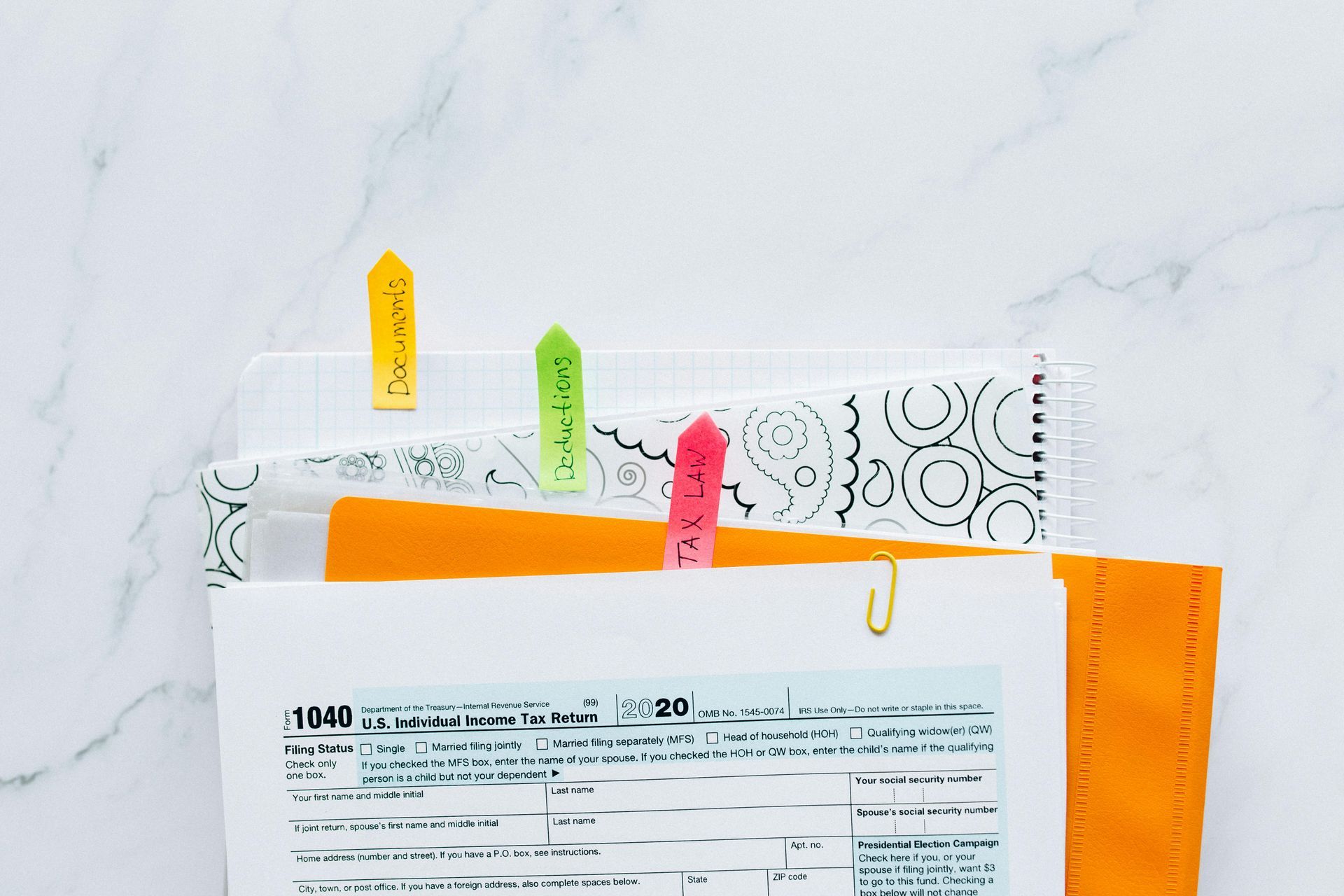 Tax forms and papers clipped with colored sticky notes on a marble surface.