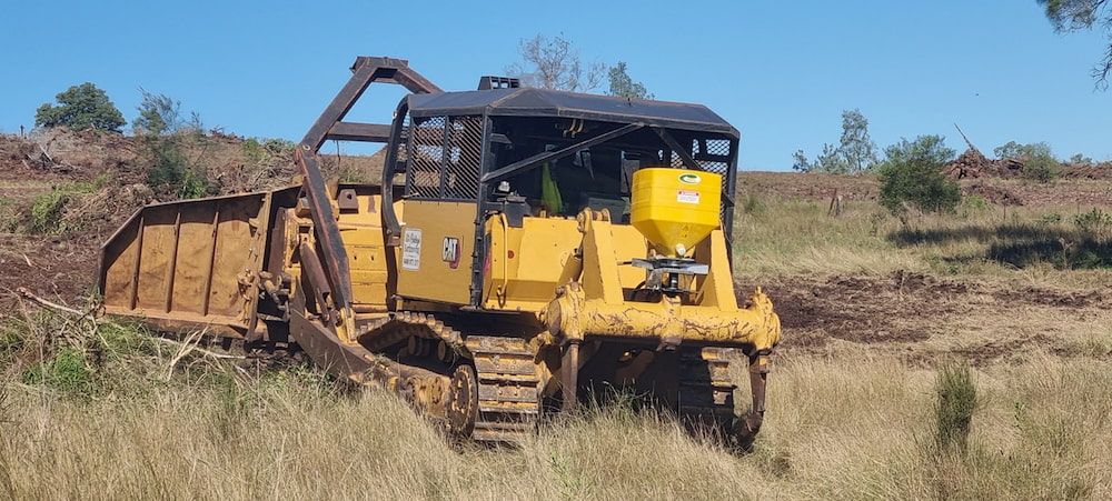 A Yellow Bulldozer is Driving Through a Grassy Field — Oakleigh Earthmoving in Cotswold Hills, QLD