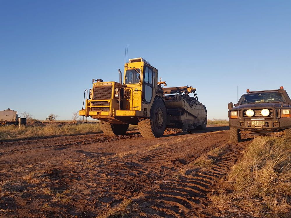 A Yellow Bulldozer is Driving Down a Dirt Road — Oakleigh Earthmoving in Kingaroy, QLD