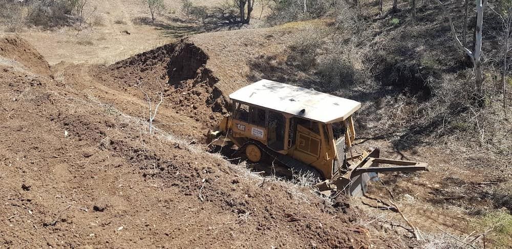 A Bulldozer is Driving Down a Dirt Road— Oakleigh Earthmoving in Dalby, QLD