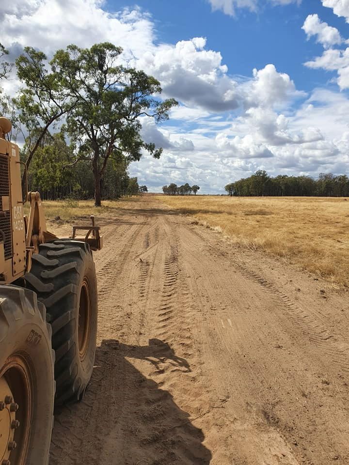 A Tractor is Driving Down a Dirt Road in a Field — Oakleigh Earthmoving in Dalby, QLD