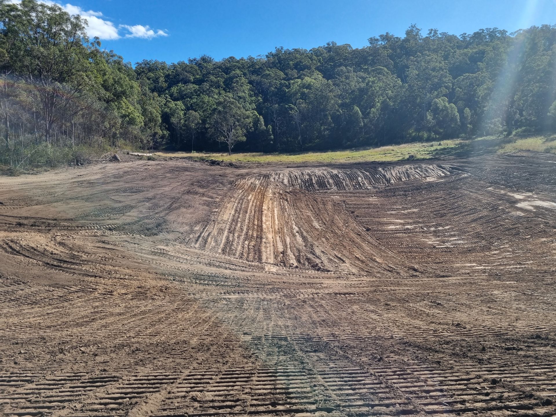 Cleared Dirt Field With Tire Tracks, Bordered by Dense Green Trees Under a Blue Sky — Oakleigh Earthmoving in Toowoomba, QLD