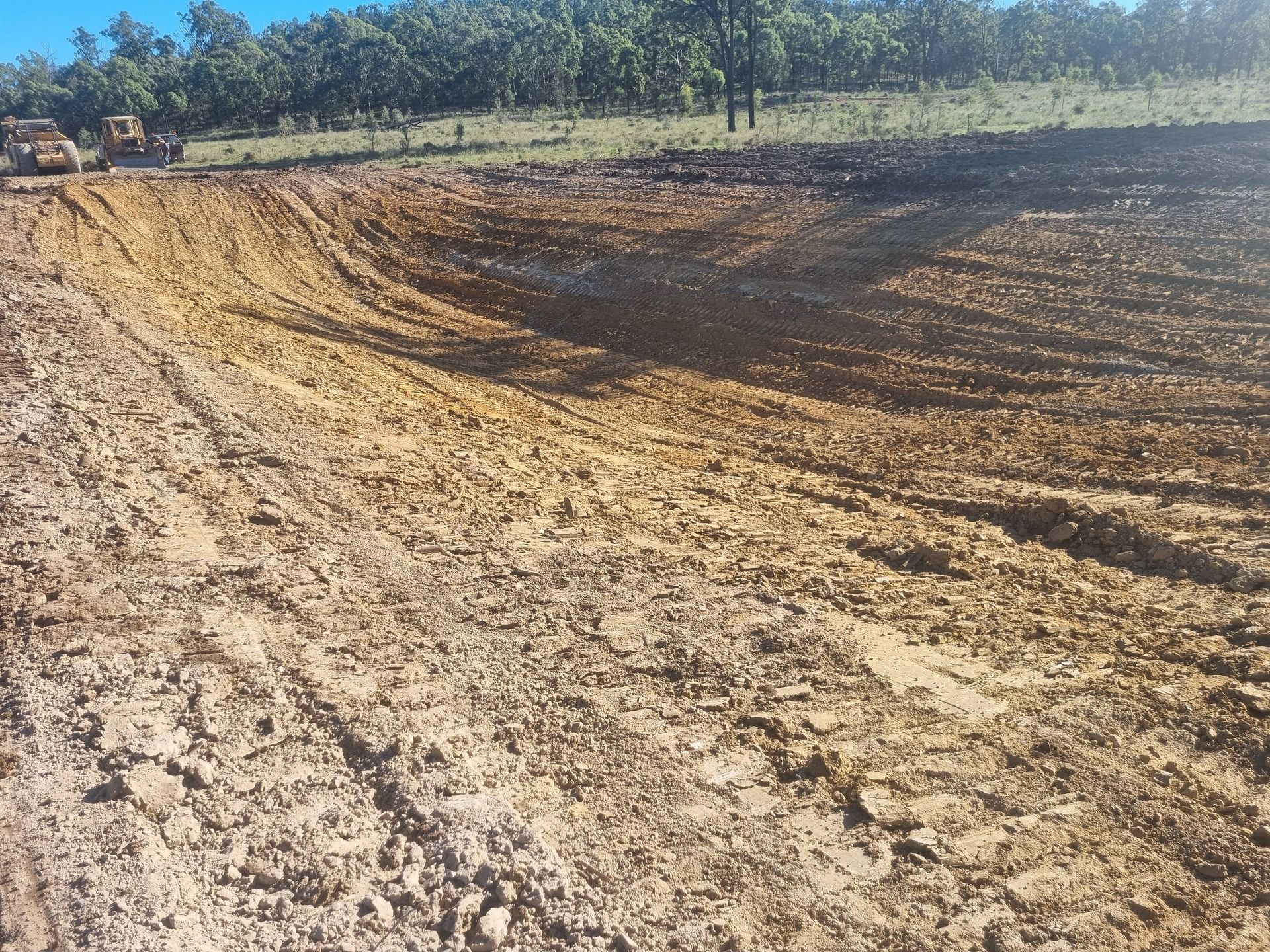 Dirt Excavation Site With a Large Curved Trench Under a Clear Sky and Trees — Oakleigh Earthmoving in Warwick, QLD