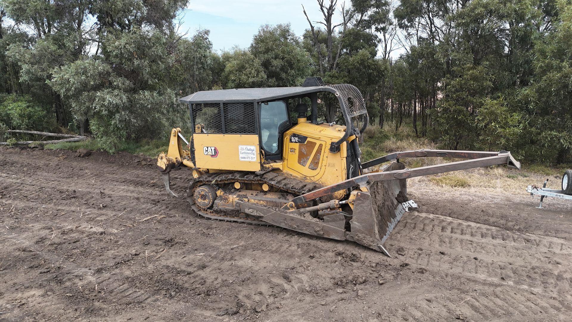 Yellow Excavator Clearing Muddy Ground Near Trees on a Work Site — Oakleigh Earthmoving in Kingaroy, QLD