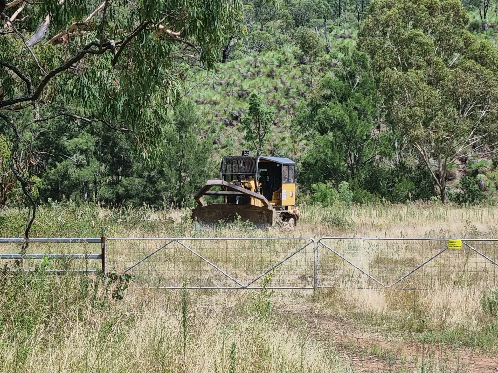 Yellow Bulldozer Behind a Wire Fence in a Grassy Field With Trees in the Background — Oakleigh Earthmoving in Toowoomba, QLD