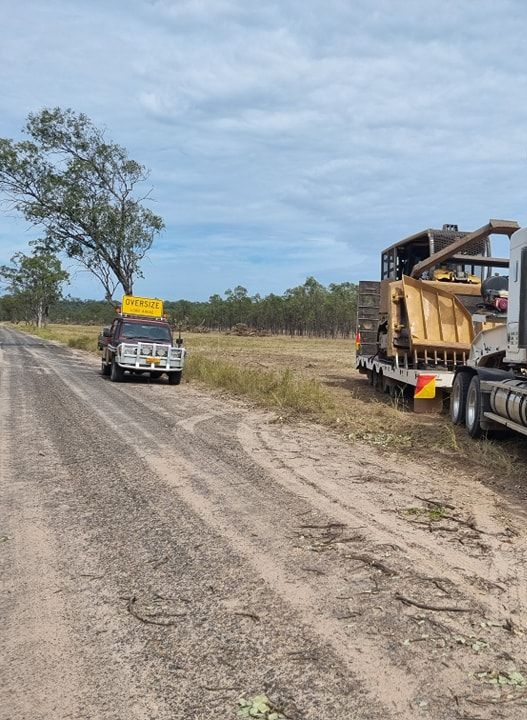 Heavy Hauling Truck With Oversize Signs Towing Machinery on a Dirt Road — Oakleigh Earthmoving in Kingaroy, QLD