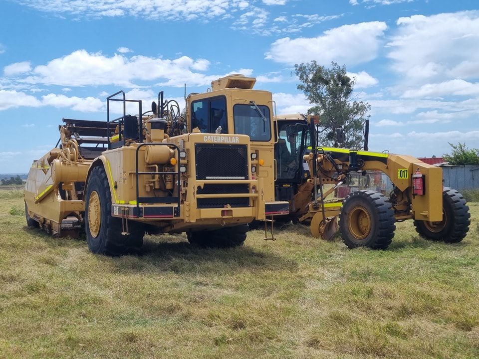 Yellow Construction Machinery Parked on a Grassy Field Under a Blue Sky — Oakleigh Earthmoving in Kingaroy, QLD
