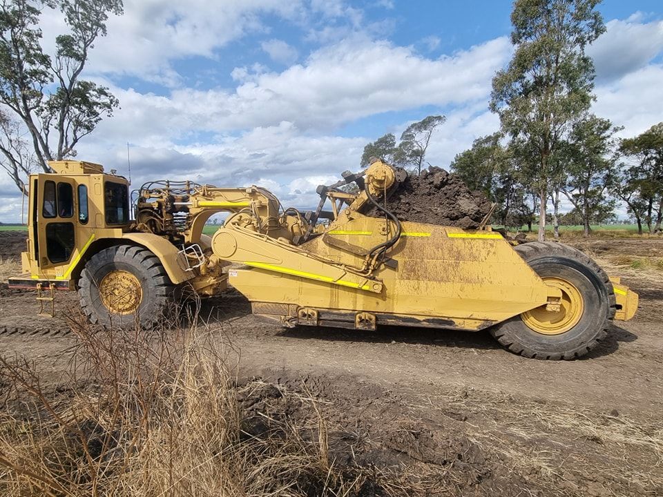 Yellow Earthmoving Scraper Hauling Dirt Across a Muddy Construction Site — Oakleigh Earthmoving in Cooyar, QLD