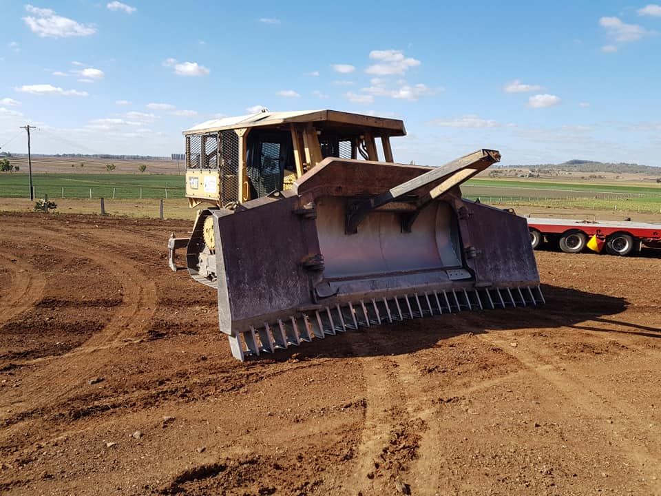 Bulldozer Leveling a Dirt Field Under a Blue Sky, With a Red Trailer — Oakleigh Earthmoving in Chinchilla, QLD