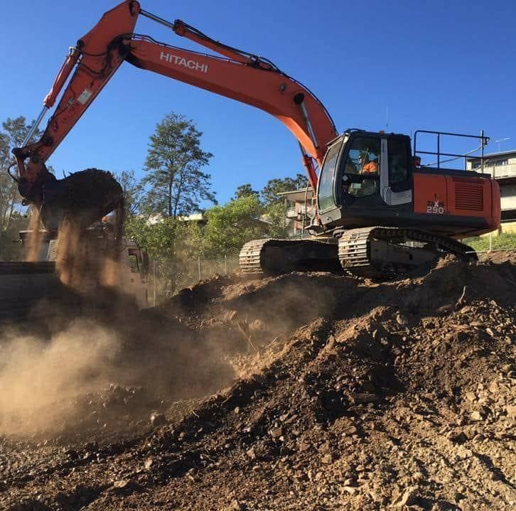 Orange Excavator Dumping Soil on a Dirt Pile Under a Clear Blue Sky — Oakleigh Earthmoving in Chinchilla, QLD