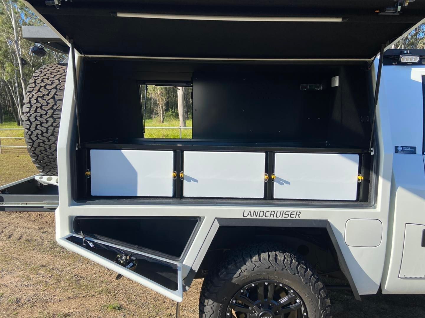 White Truck Bed With a Canopy, Storage Drawers, and a Spare Tire. Black Cargo Rack Mounted on a Vehicle Roof — Custom RV Creations in Ipswich, QLD